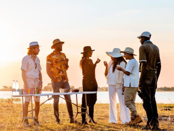 Friends gathering around a table with drinks at sunset.