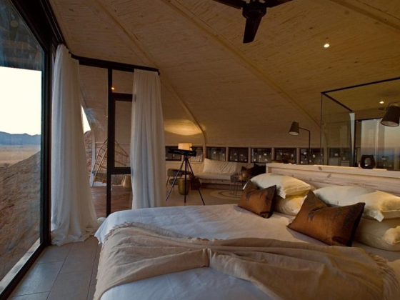 Cozy interior featuring a bed and telescope in a desert setting.